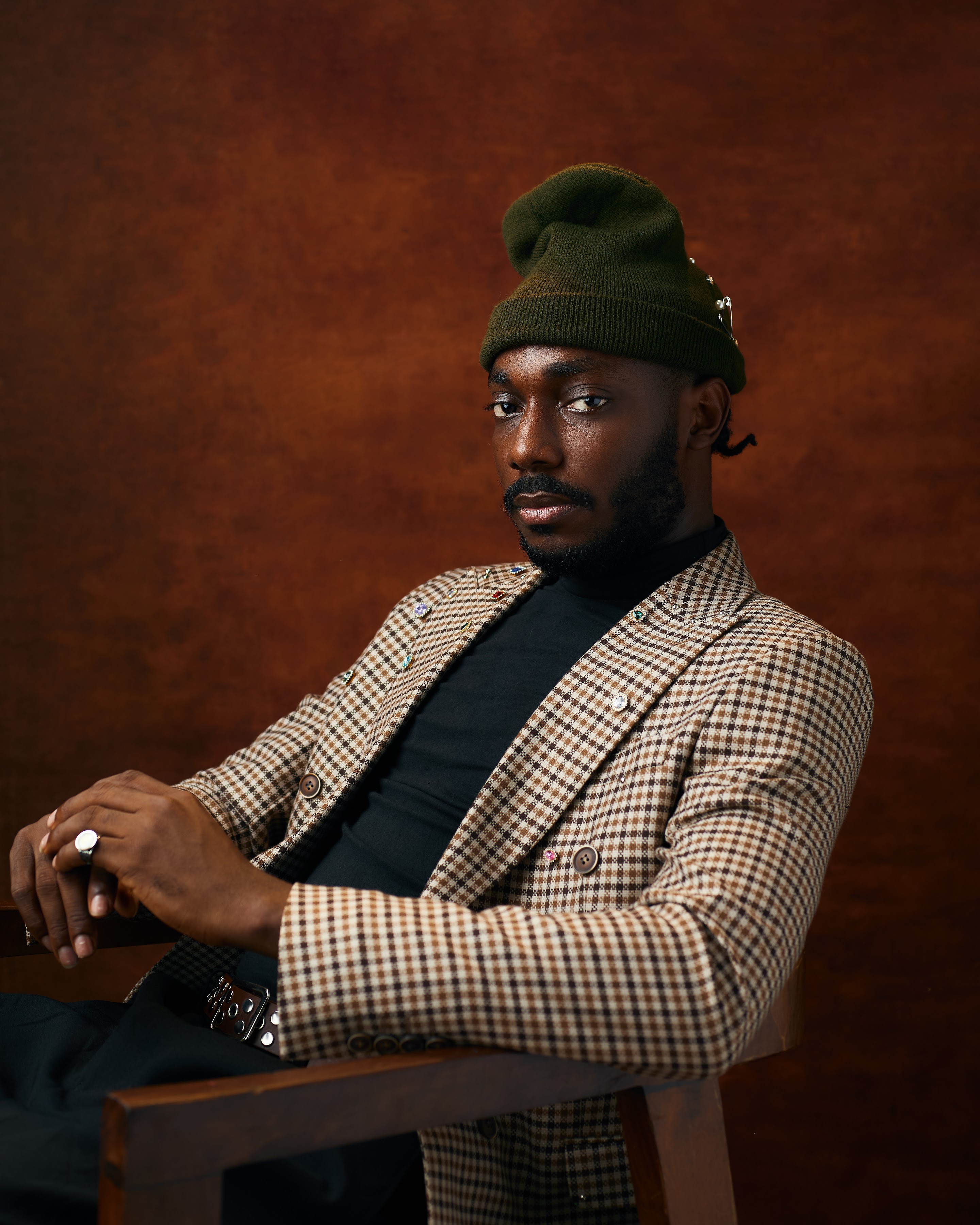 Saelem in a houndstooth blazer and olive beanie, seated