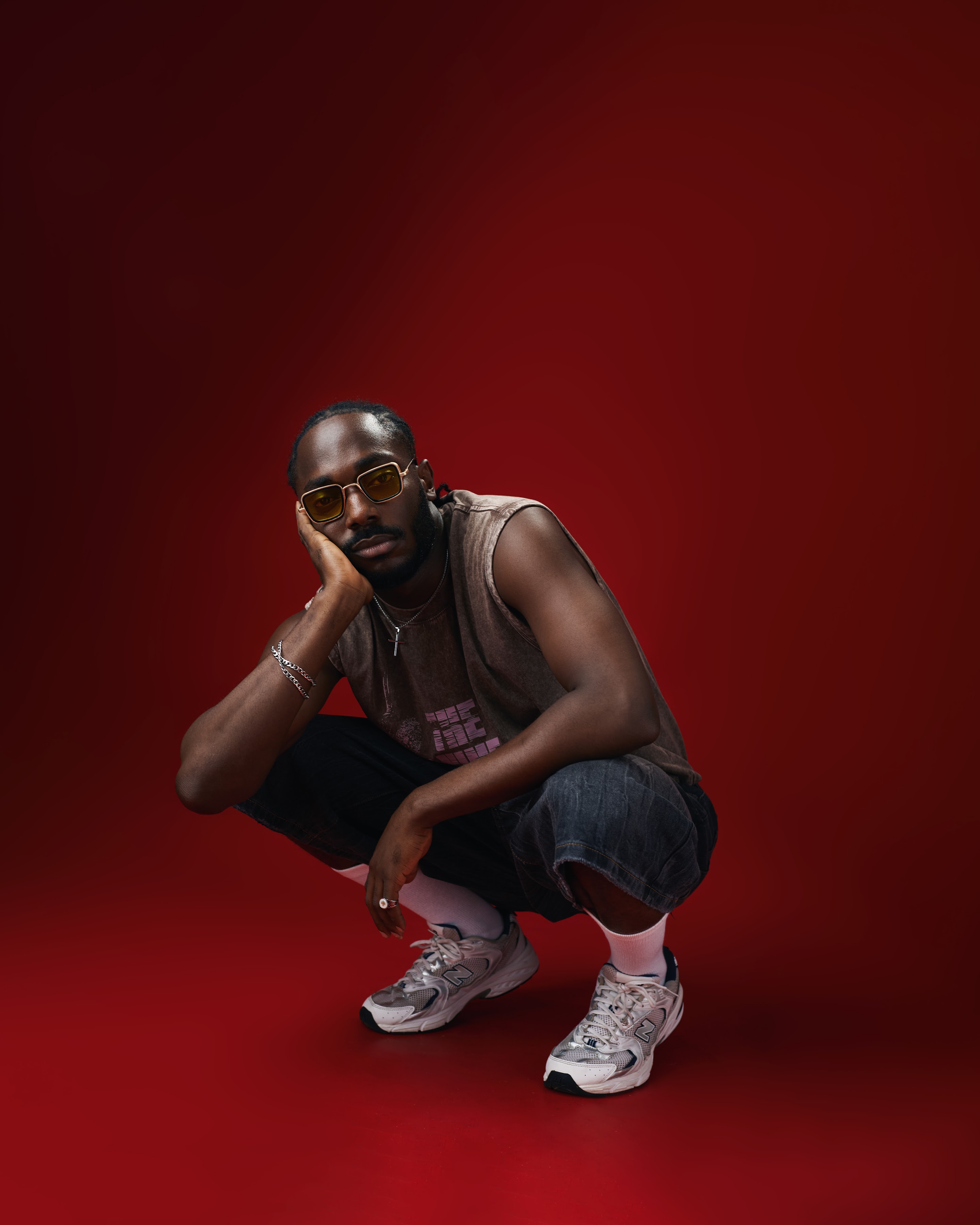 Saelem crouching in white sneakers on a red studio floor