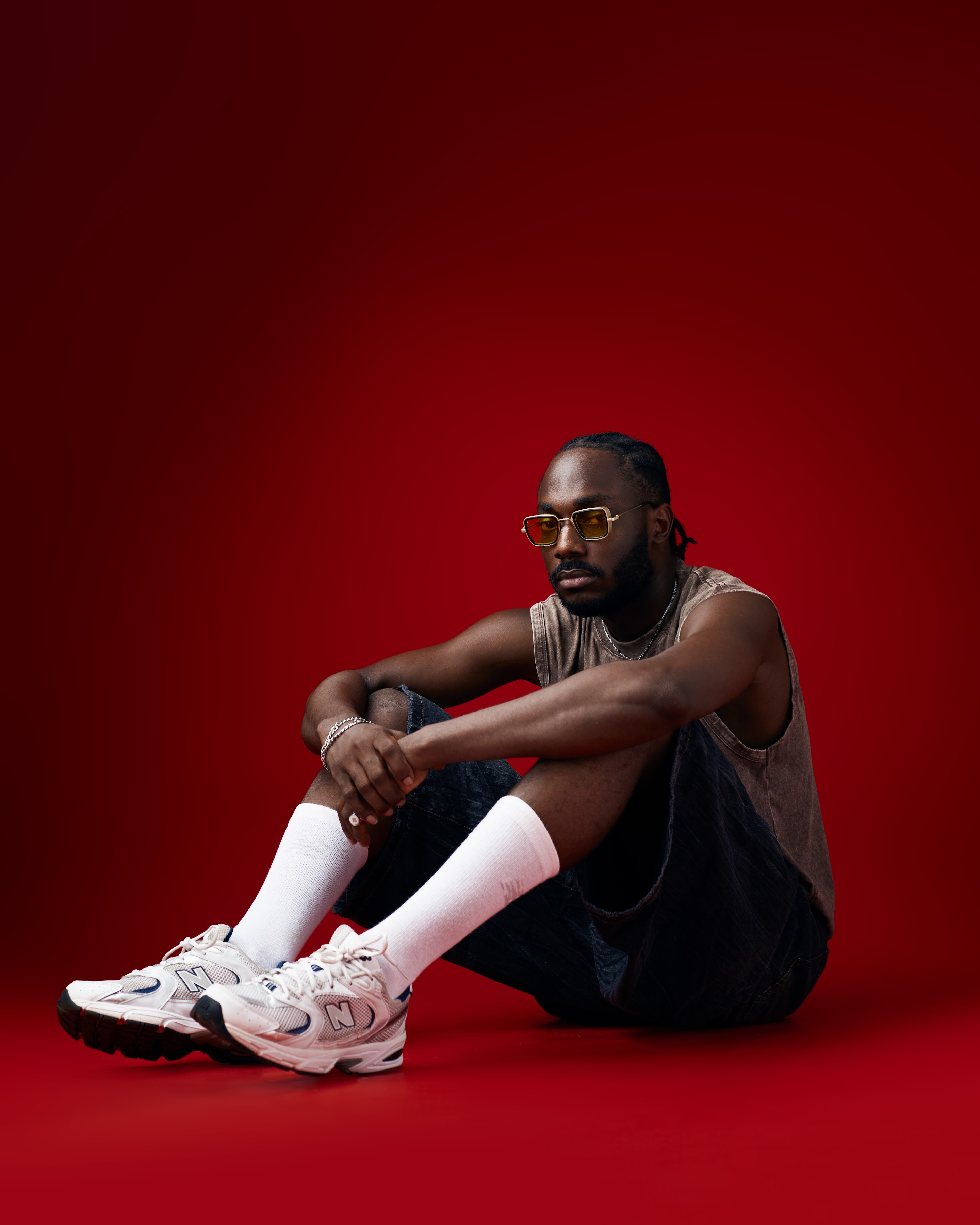 Saelem seated on a red studio floor in amber sunglasses