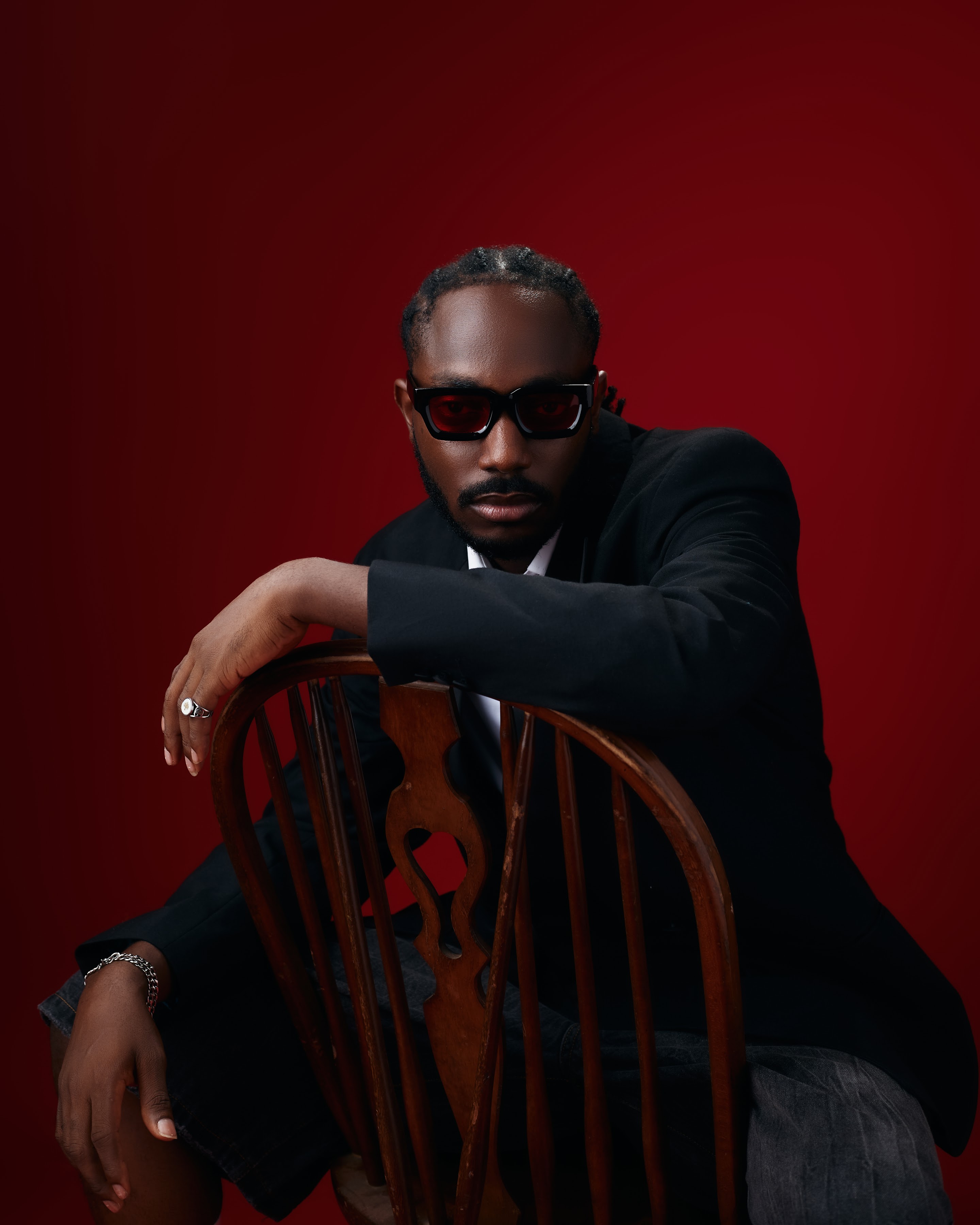 Saelem leaning on a wooden chair in dark sunglasses